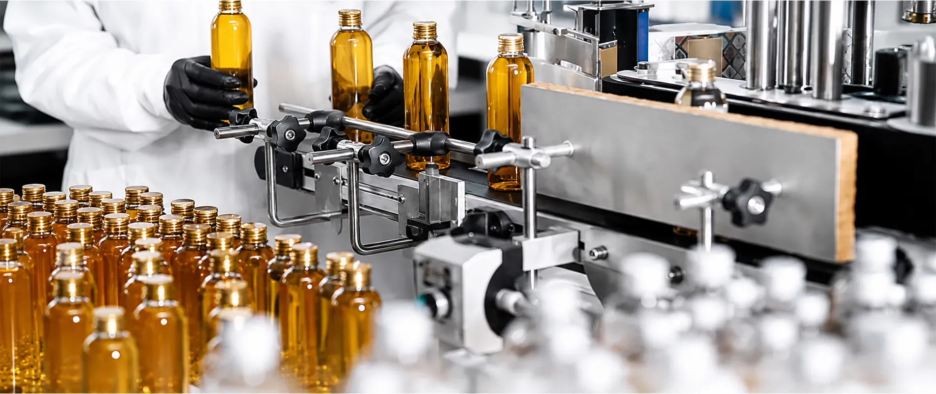 Cosmetic manufacturing production line with amber glass bottles being filled and inspected by technicians in a controlled facility, highlighting quality control and automated packaging processes.