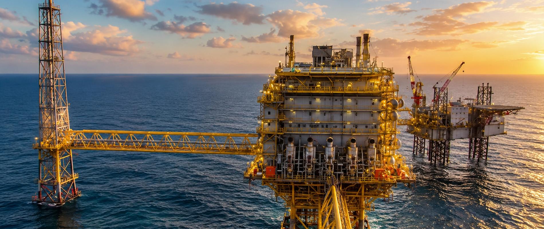 Offshore oil and gas production platform in the ocean with illuminated facilities and flare stack at sunset